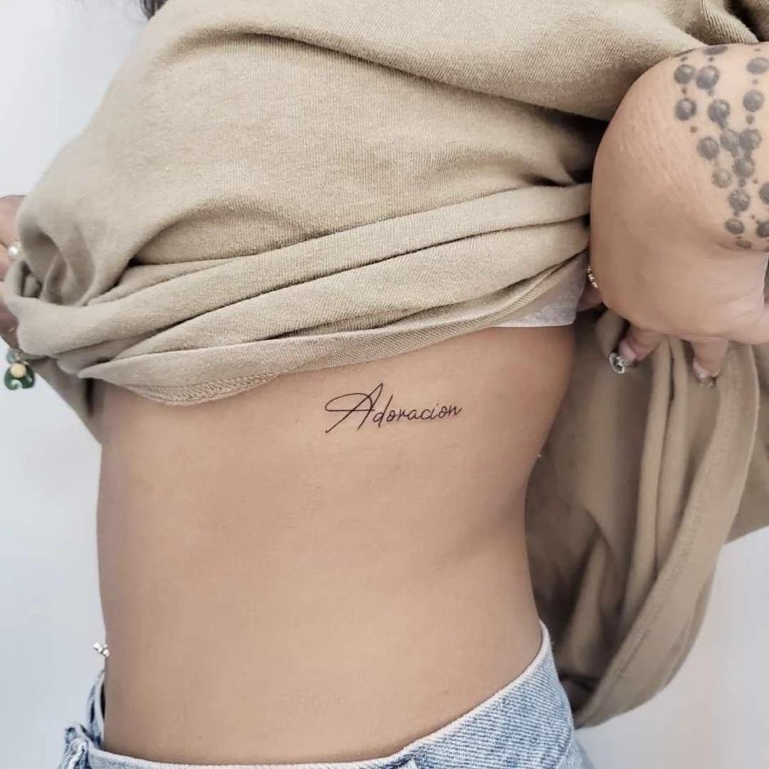 Tattoo on the side of a person's torso that reads 'Adoracion'
