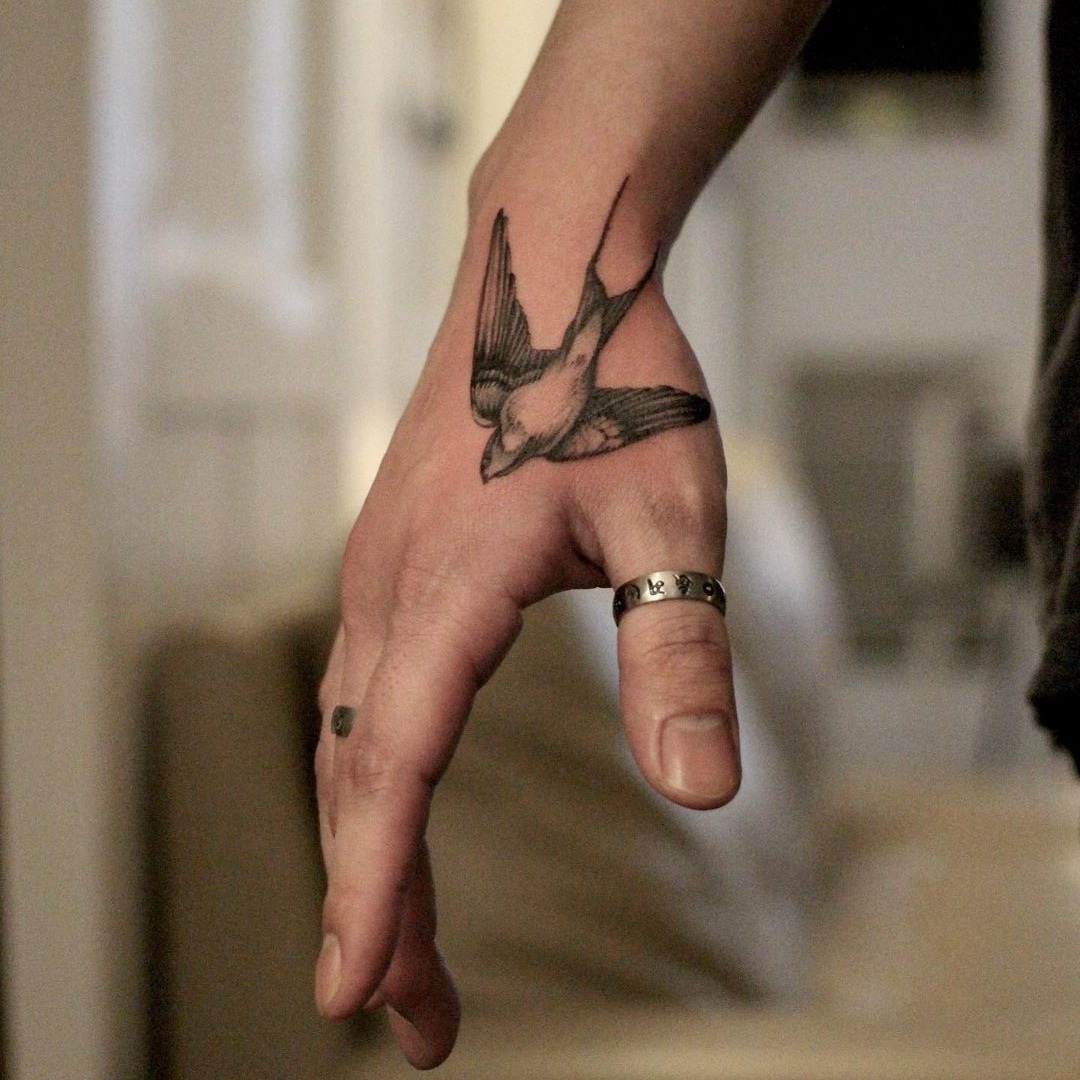 A tattoo of a bird on a person's hand.