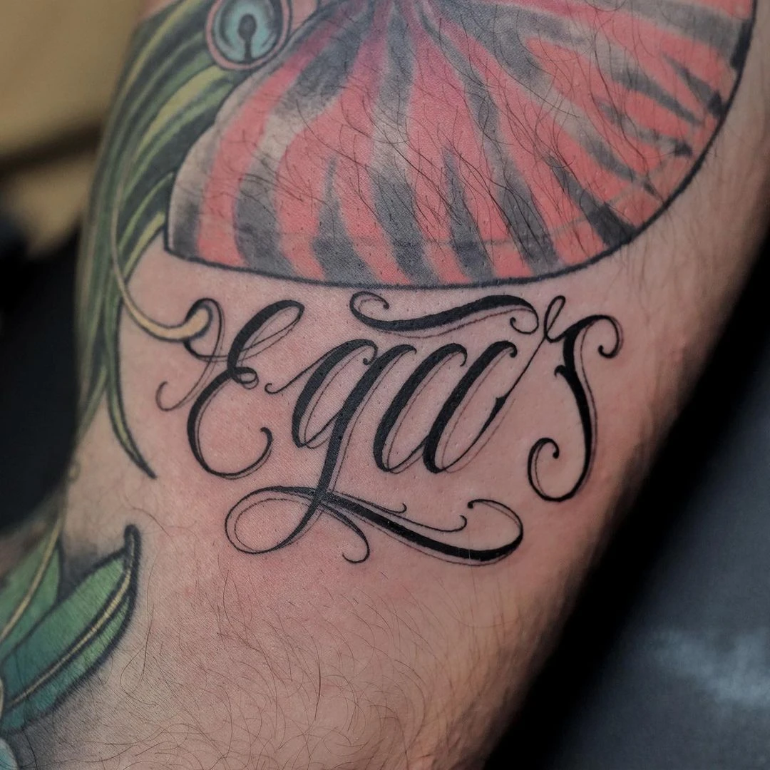 Intricate tattoo featuring the word 'equals' in cursive on a forearm, surrounded by colorful leaves.