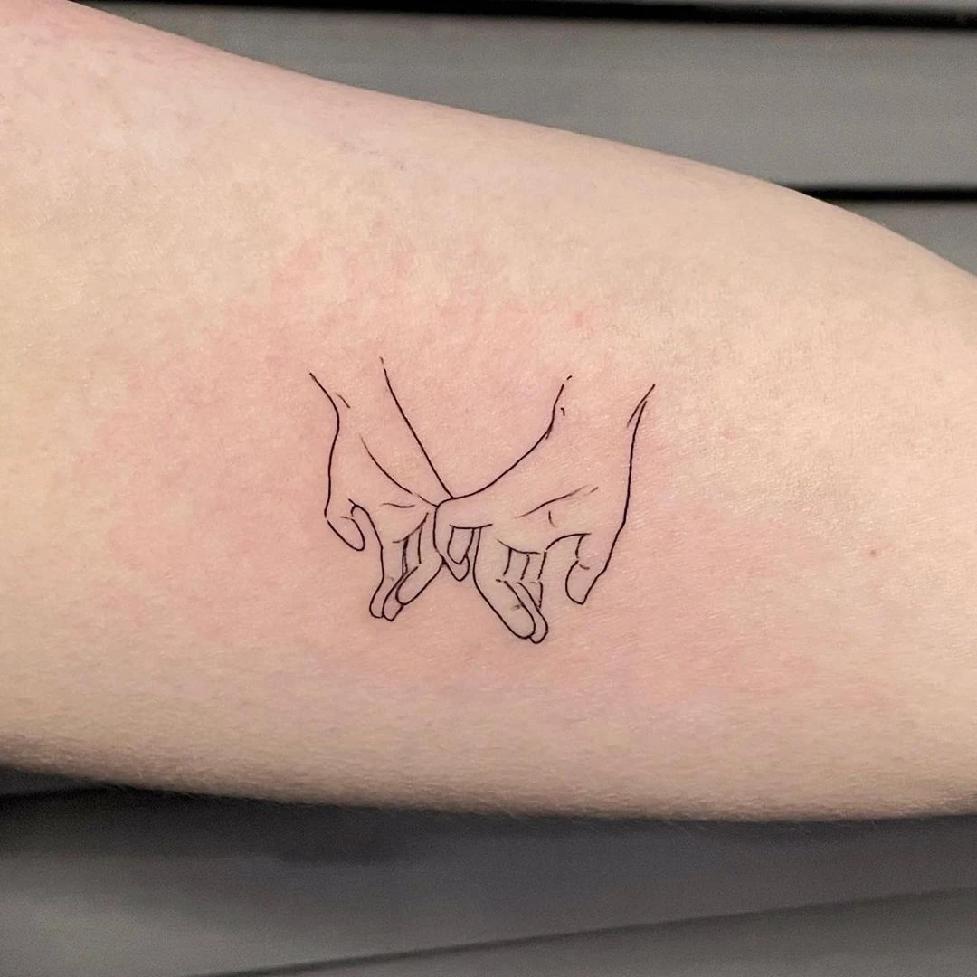 Delicate tattoo of two hands interlocking fingers