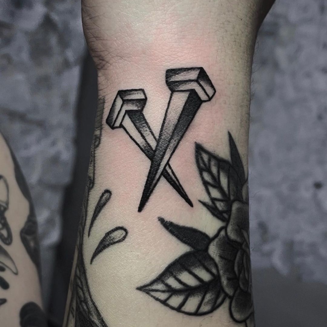 Tattoo featuring two stylized black nails on skin.