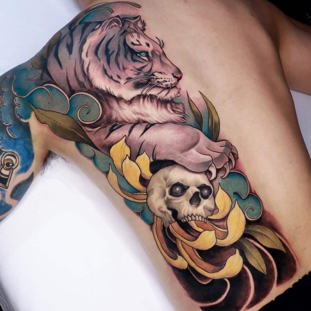Tattoo of a tiger, skull, and flowers on side torso.